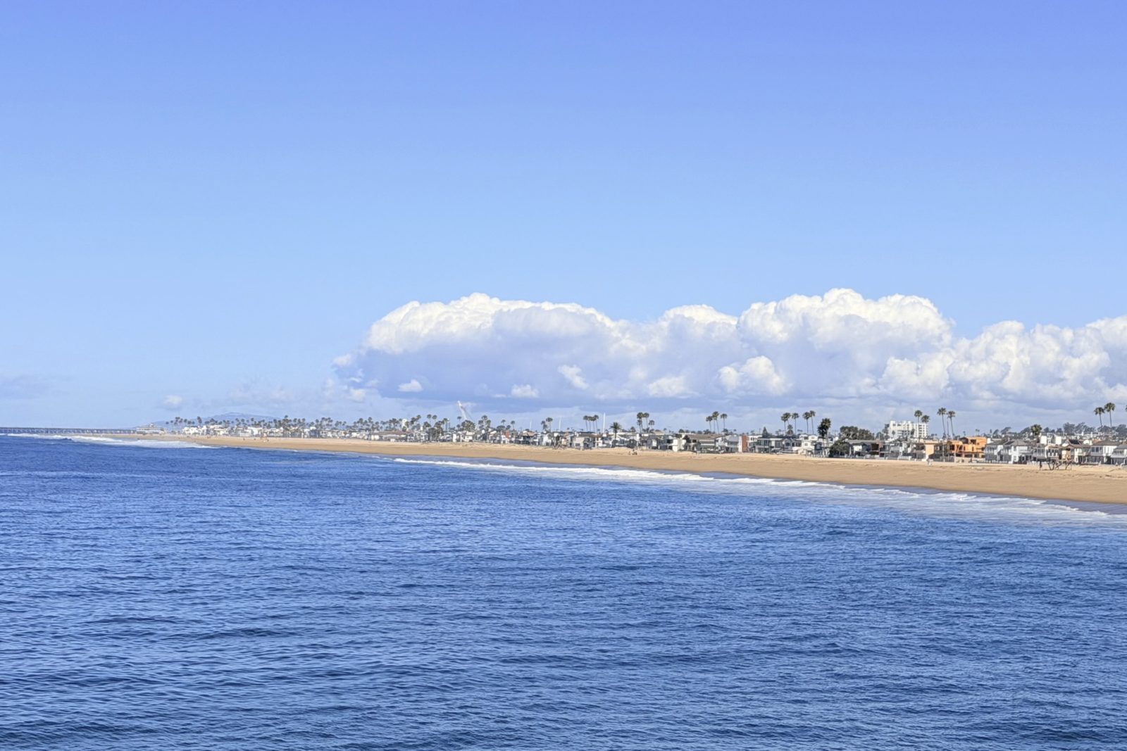 Orange County shoreline with beachfront homes along the sand and a pier in the distance